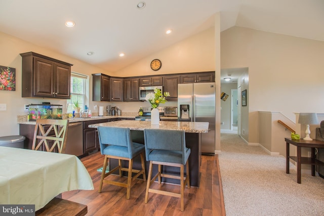 kitchen featuring dark brown cabinets, light stone countertops, appliances with stainless steel finishes, a kitchen bar, and a kitchen island