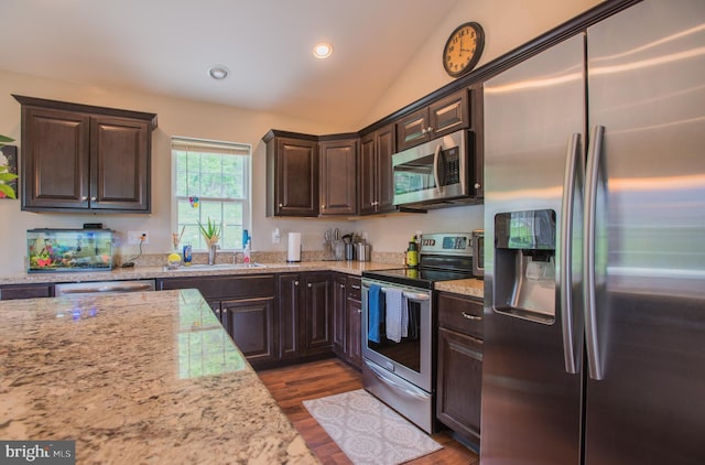 kitchen featuring appliances with stainless steel finishes, vaulted ceiling, dark brown cabinets, a sink, and dark wood-style floors