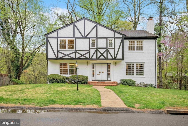 tudor house featuring brick siding, a chimney, and a front yard