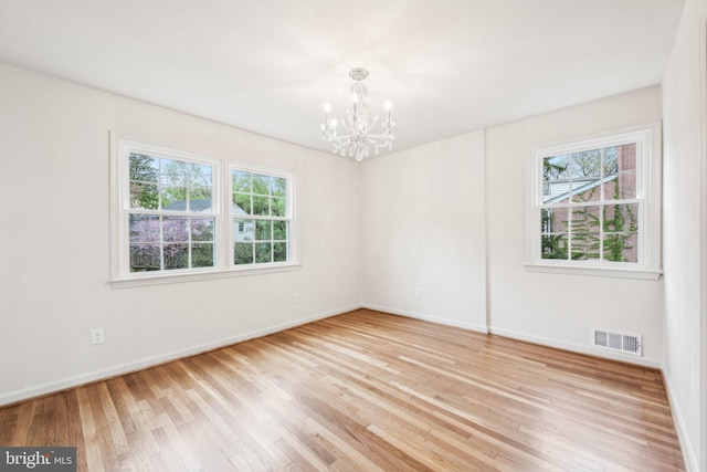 unfurnished room with visible vents, light wood-type flooring, a wealth of natural light, and an inviting chandelier