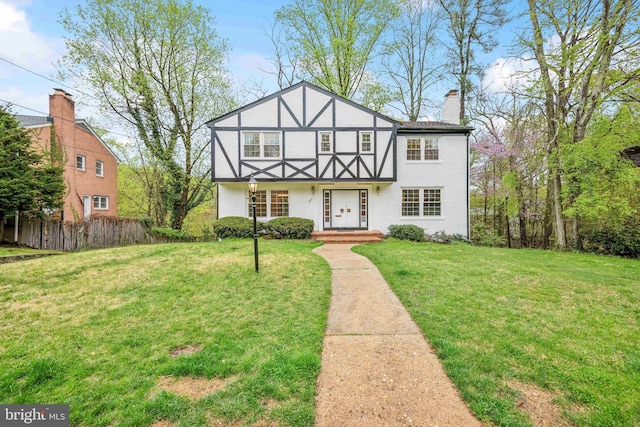 tudor-style house with a front lawn, fence, and a chimney