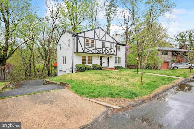 tudor house with an attached garage, a front lawn, driveway, and a chimney