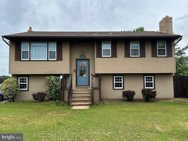 raised ranch with stucco siding, a chimney, and a front lawn