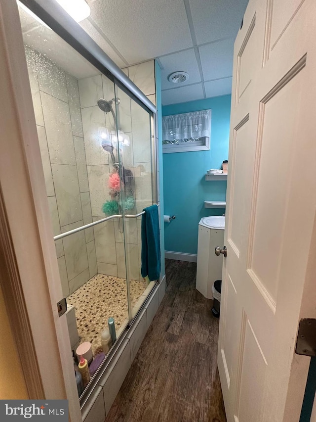 bathroom with a paneled ceiling, baseboards, wood finished floors, and a stall shower