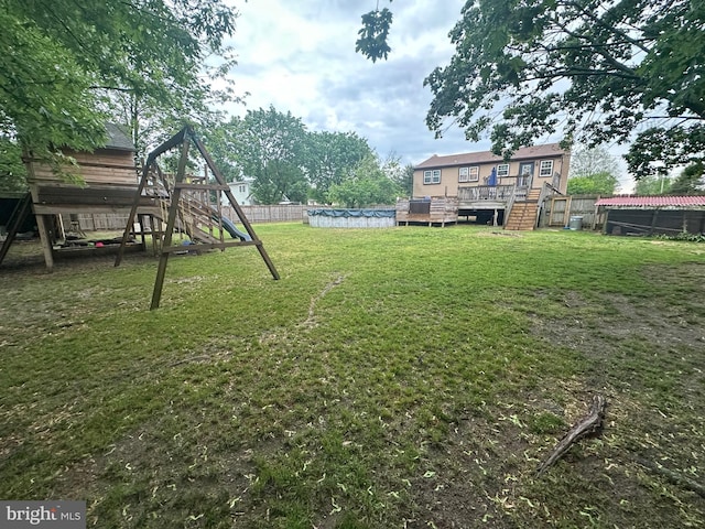 view of yard featuring a fenced backyard, a playground, a wooden deck, and a covered pool