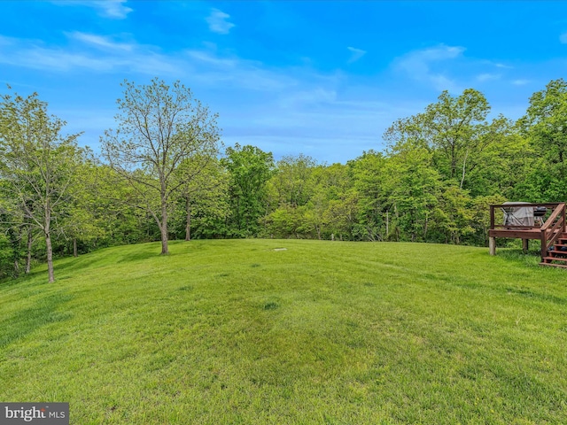 view of green lawn with a deck and a view of trees