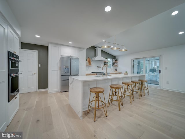 1782 Shaftsbury Ave, Crofton, MD 21114 - kitchen with stainless steel fridge with ice dispenser, wall chimney range hood, double oven, light wood finished floors, and a kitchen breakfast bar