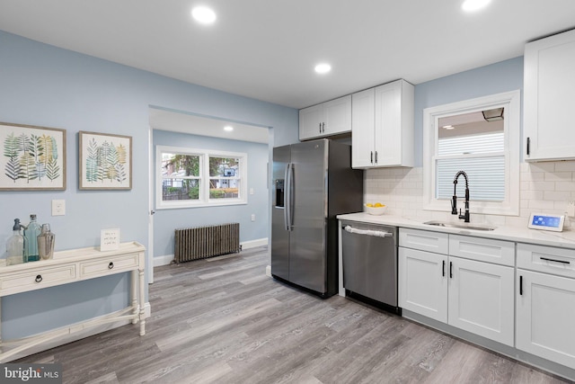 kitchen with radiator, a sink, light wood-style floors, stainless steel appliances, and white cabinets
