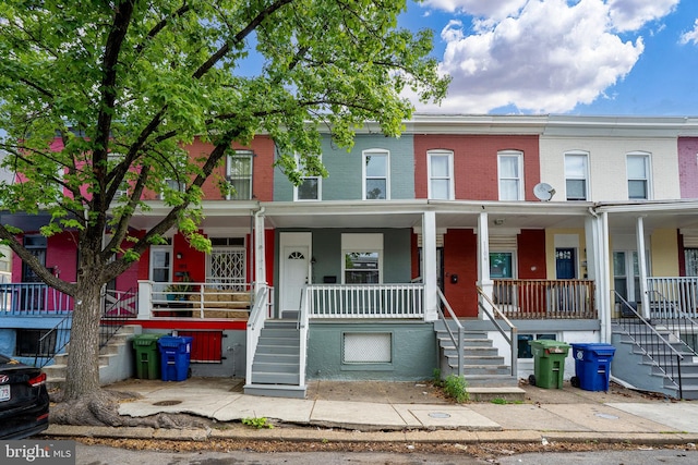 townhome / multi-family property with a porch, brick siding, and stairs