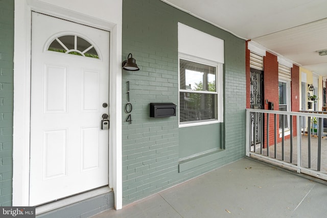 entrance to property featuring a porch and brick siding