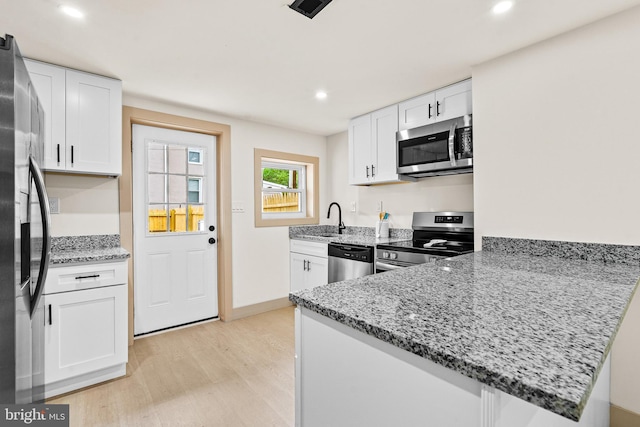 kitchen featuring light stone counters, white cabinets, stainless steel appliances, and light wood-type flooring
