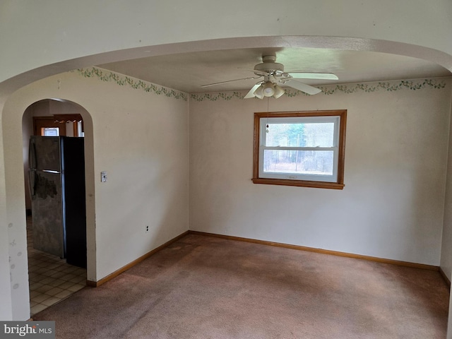 spare room featuring carpet floors, arched walkways, baseboards, and ceiling fan
