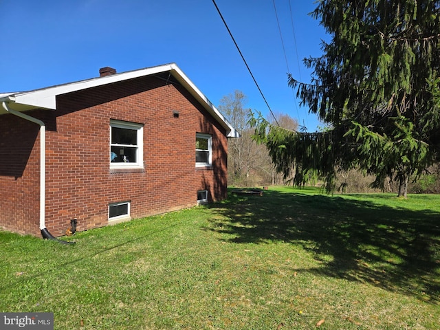 view of property exterior with brick siding, a yard, and a chimney