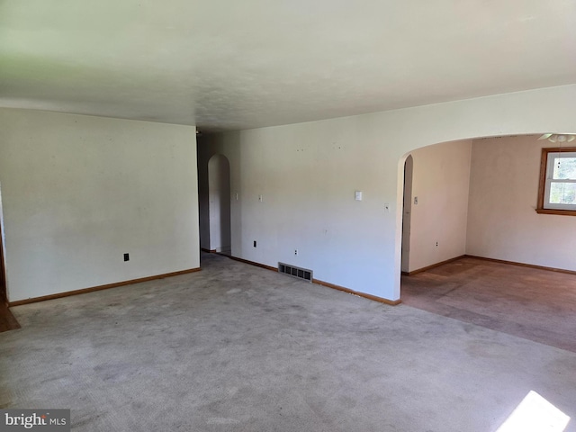unfurnished room featuring visible vents, arched walkways, and carpet