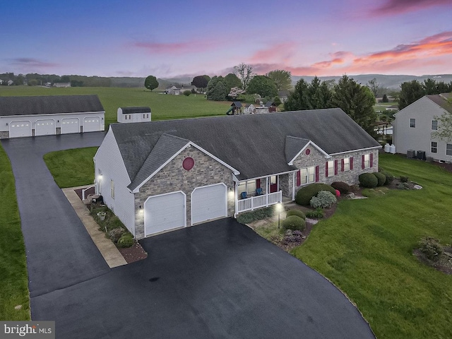 view of front of house with stone siding, covered porch, a lawn, an attached garage, and asphalt driveway
