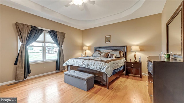 bedroom with light wood-type flooring, baseboards, a tray ceiling, and a ceiling fan