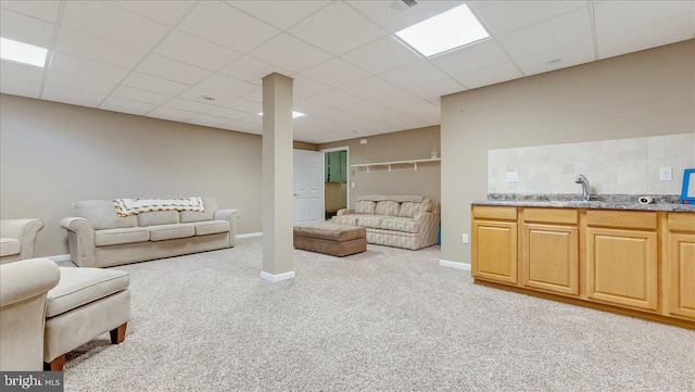 carpeted living room featuring a drop ceiling, baseboards, and a sink