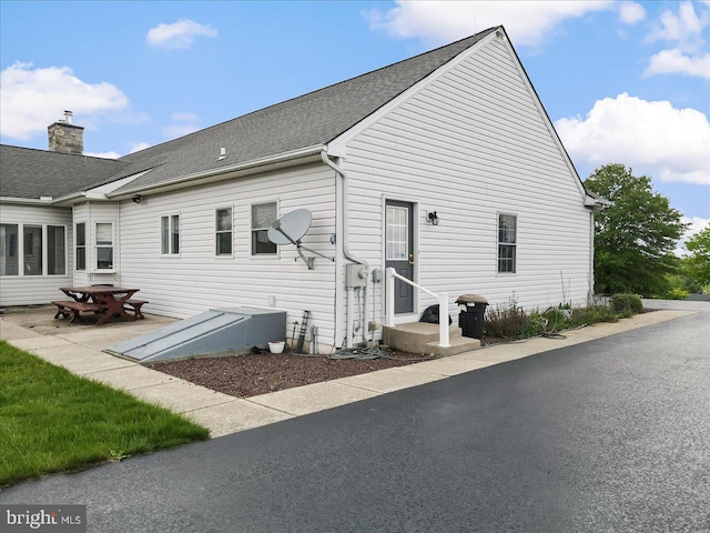 back of house featuring a shingled roof and a chimney