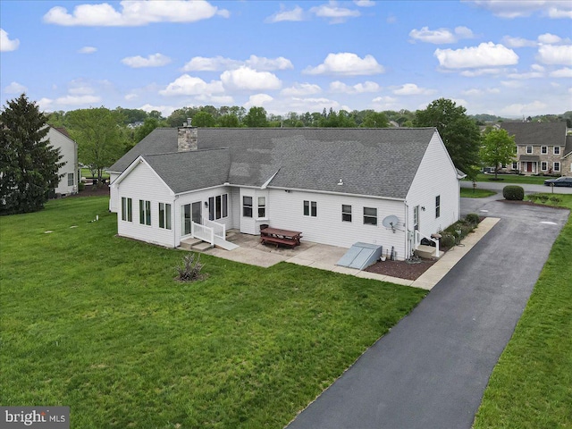 back of property featuring entry steps, a shingled roof, a lawn, and a patio
