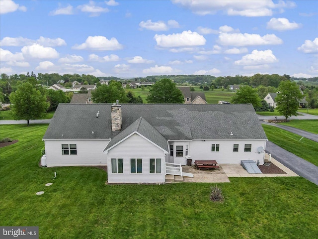 rear view of property with a lawn, a patio, a chimney, and roof with shingles