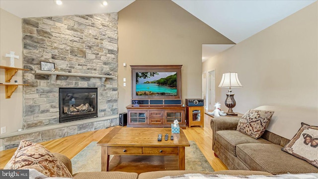 living area featuring wood finished floors, a stone fireplace, and high vaulted ceiling