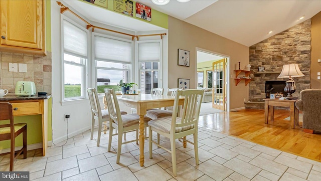 dining room with vaulted ceiling, a stone fireplace, and baseboards