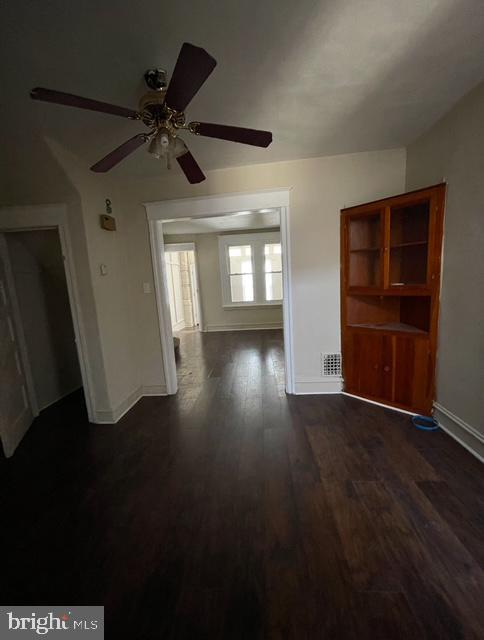 interior space featuring baseboards, a ceiling fan, and dark wood-style flooring