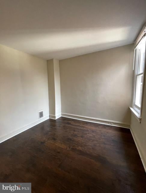 empty room with visible vents, dark wood finished floors, baseboards, and a healthy amount of sunlight