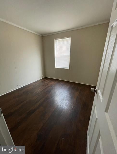 empty room with baseboards, ornamental molding, and dark wood-type flooring