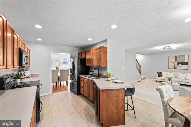 kitchen with black appliances, open floor plan, a breakfast bar, a sink, and brown cabinetry