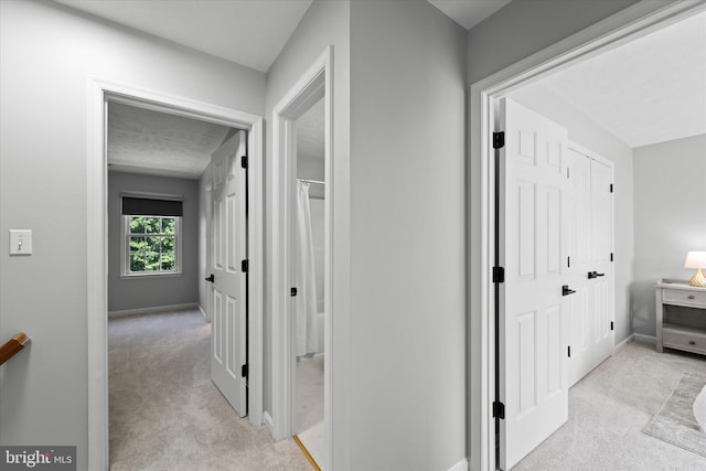hallway featuring light carpet and baseboards