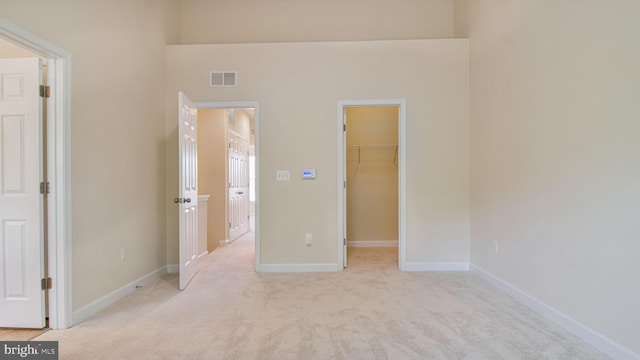 unfurnished bedroom with a walk in closet, light colored carpet, baseboards, and a closet