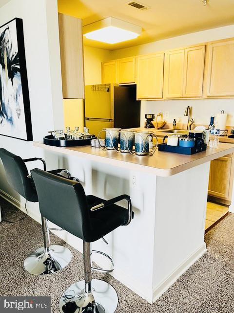 9000 Bay Ave Unit 209, North Beach, MD 20714 - kitchen featuring light countertops, a breakfast bar area, freestanding refrigerator, light brown cabinetry, and baseboards