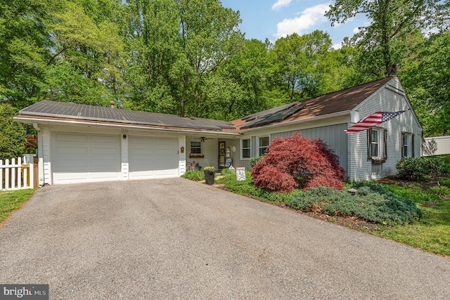 single story home featuring an attached garage, roof mounted solar panels, driveway, and fence