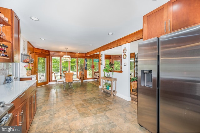 kitchen featuring brown cabinets, stone finish flooring, stainless steel refrigerator with ice dispenser, baseboards, and recessed lighting