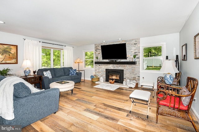 living area featuring a fireplace, wood-type flooring, baseboards, and a healthy amount of sunlight