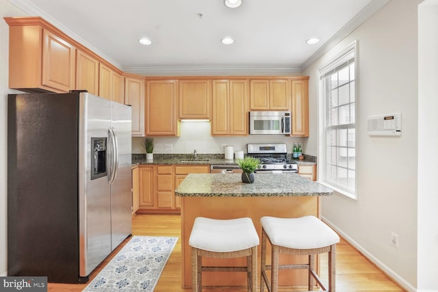 kitchen with appliances with stainless steel finishes, ornamental molding, a sink, light wood finished floors, and a center island