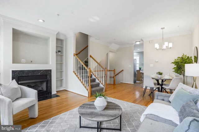 living area with stairway, wood finished floors, a premium fireplace, crown molding, and a chandelier