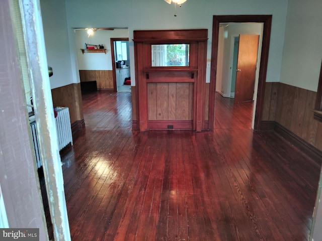 hallway featuring wood-type flooring, a wainscoted wall, wooden walls, and radiator