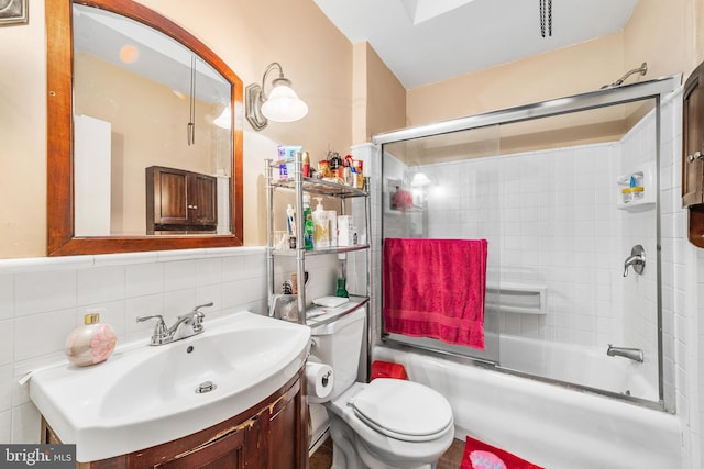 full bathroom with enclosed tub / shower combo, vanity, toilet, and tile walls