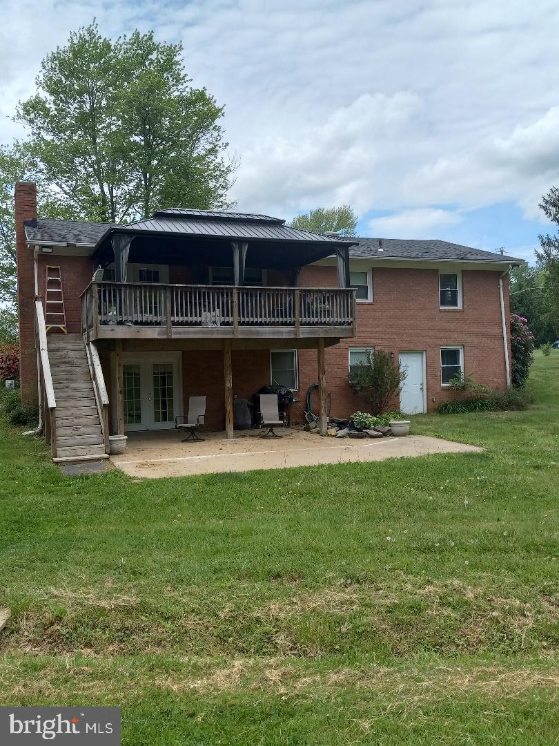 back of property featuring a deck, a patio, stairway, a chimney, and a lawn