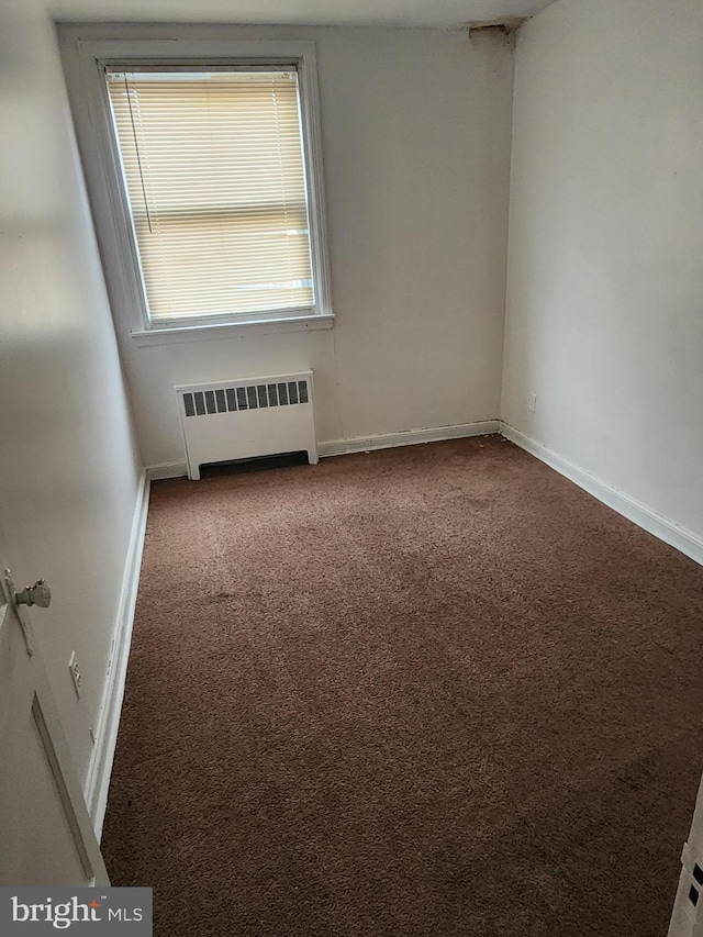 empty room with carpet floors, baseboards, and radiator heating unit