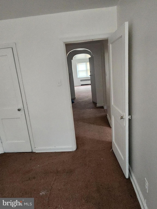 corridor featuring arched walkways, baseboards, and dark carpet