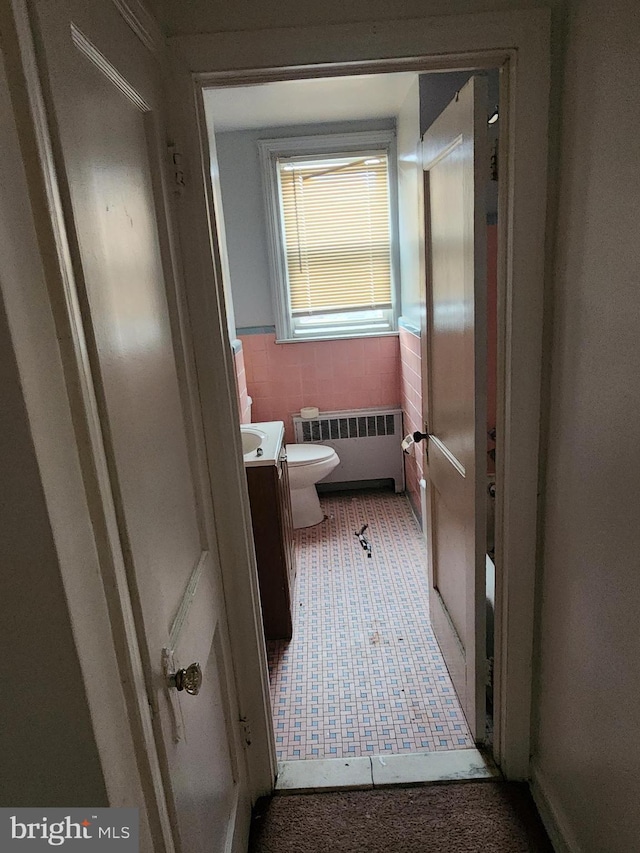 bathroom featuring vanity, radiator, toilet, tile walls, and tile patterned floors