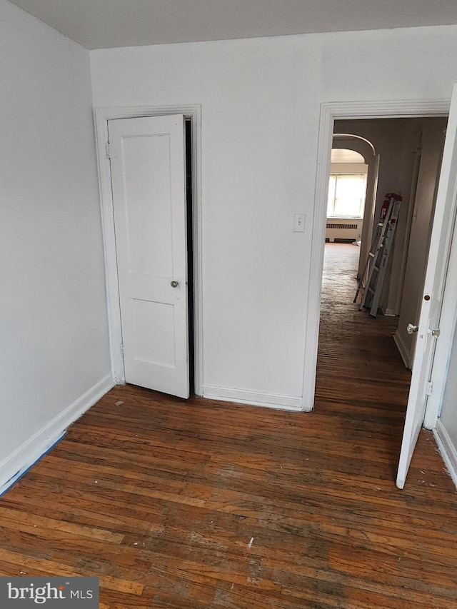 unfurnished bedroom with baseboards, arched walkways, and dark wood finished floors