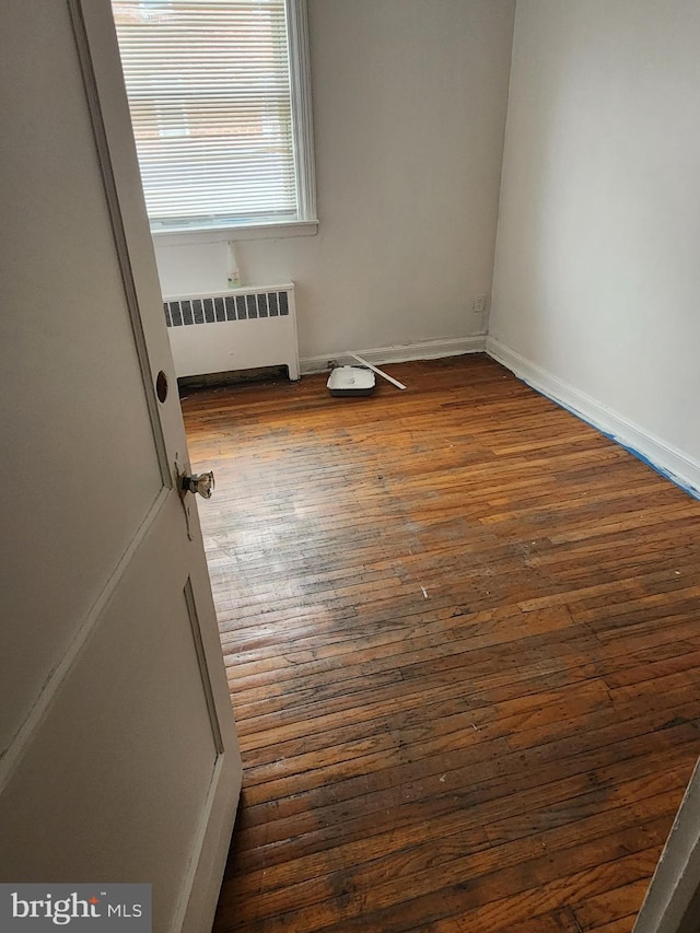 empty room featuring dark wood-style flooring, baseboards, and radiator