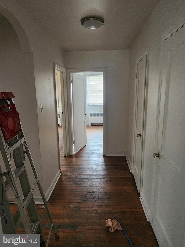 hall featuring baseboards, arched walkways, dark wood-style flooring, and radiator heating unit