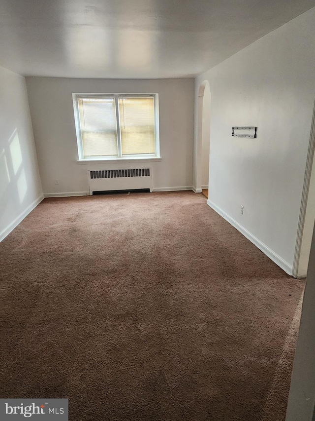 carpeted spare room featuring radiator, baseboards, and arched walkways