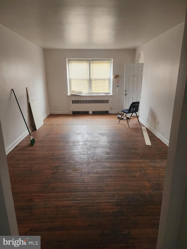 empty room featuring baseboards, dark wood-style floors, and radiator