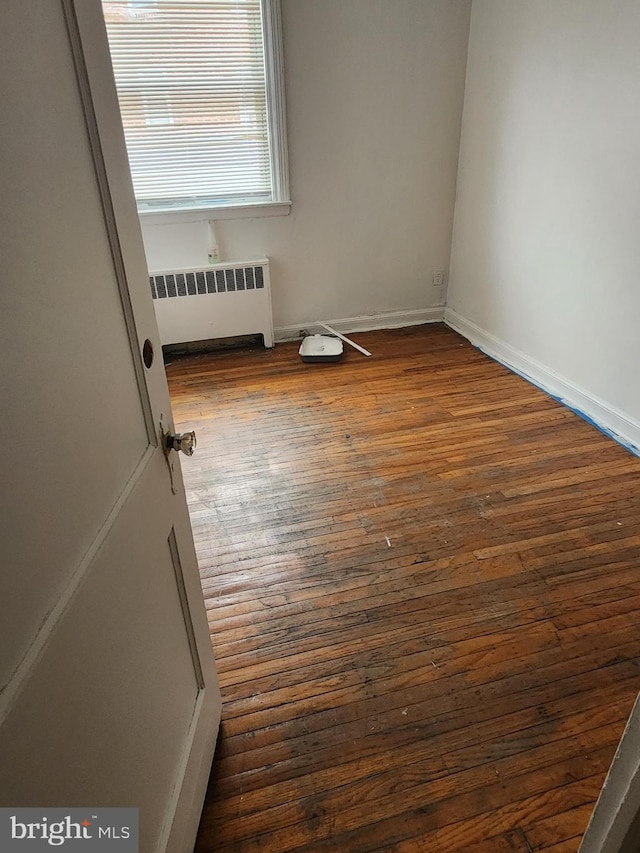 spare room with baseboards, radiator heating unit, and dark wood-type flooring